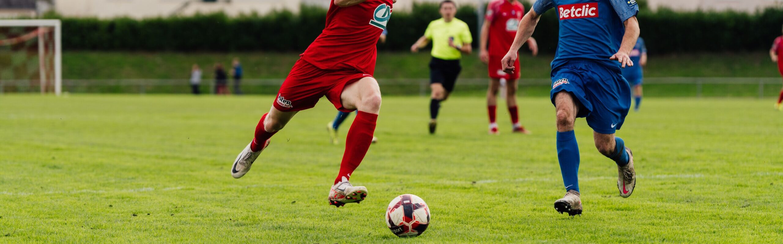 Action shot of soccer players competing on a lush green field outdoors.